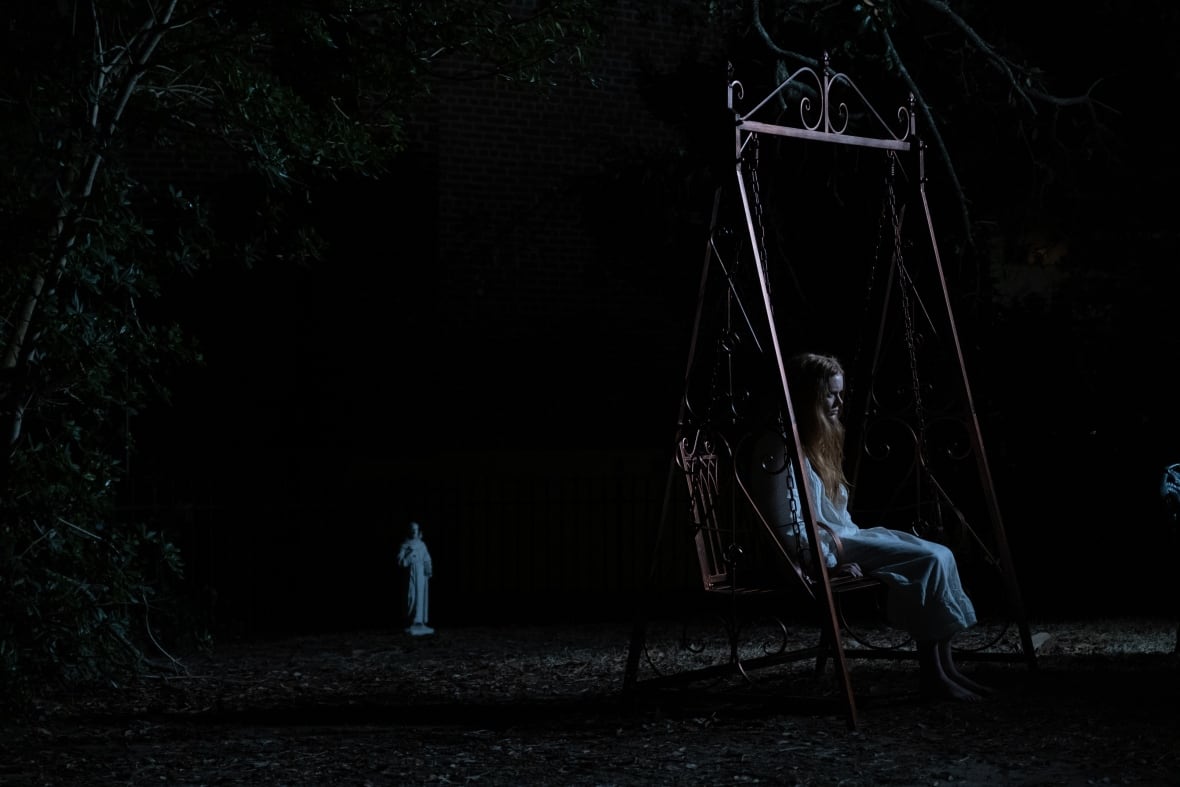 A woman sits on a swing in the dark.