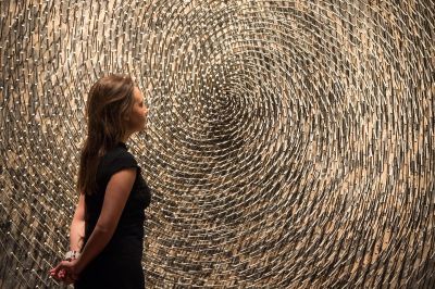 A woman standing in front of a work made from nails arranged in a spiral-like shape.