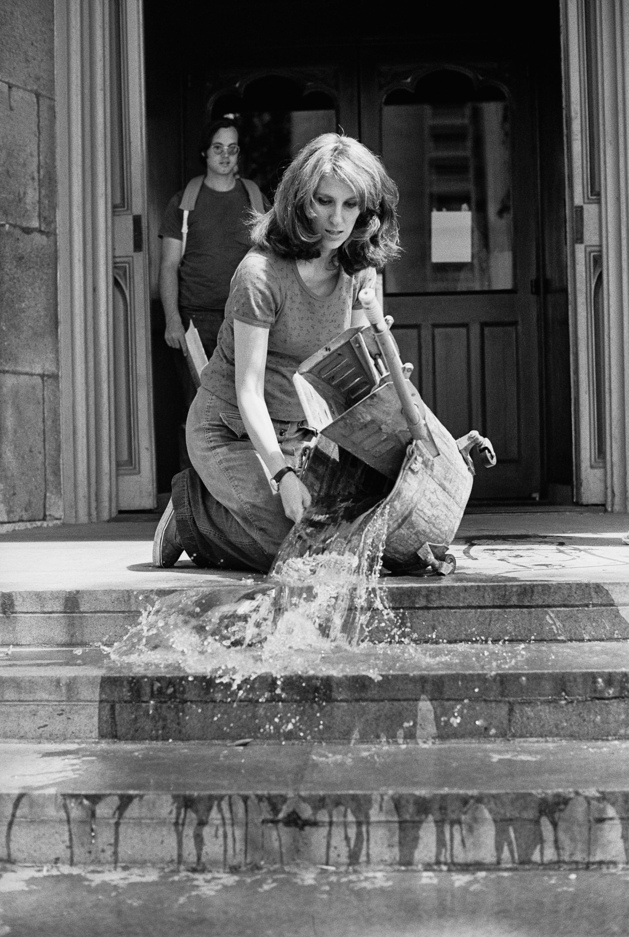 a black and white phoot of a woman dumping water down steps
