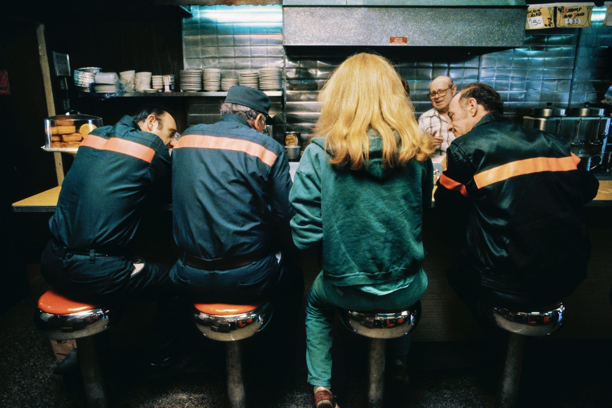the backs of three men and a blonde woman sitting at a lunch counter