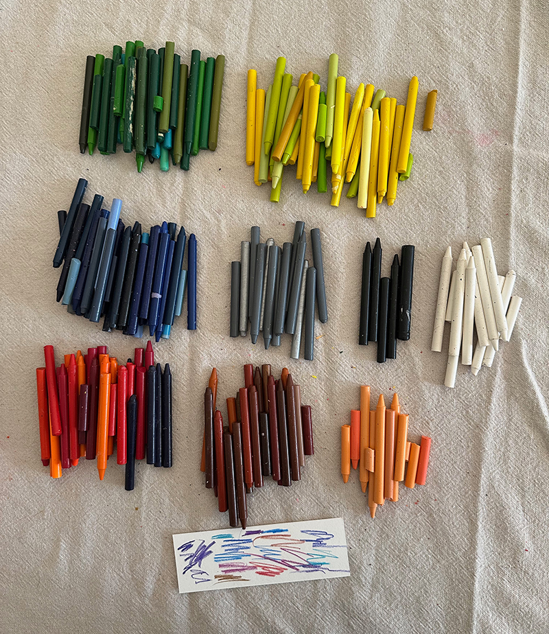 Old, unpeeled crayons on a table sorted by colors families.