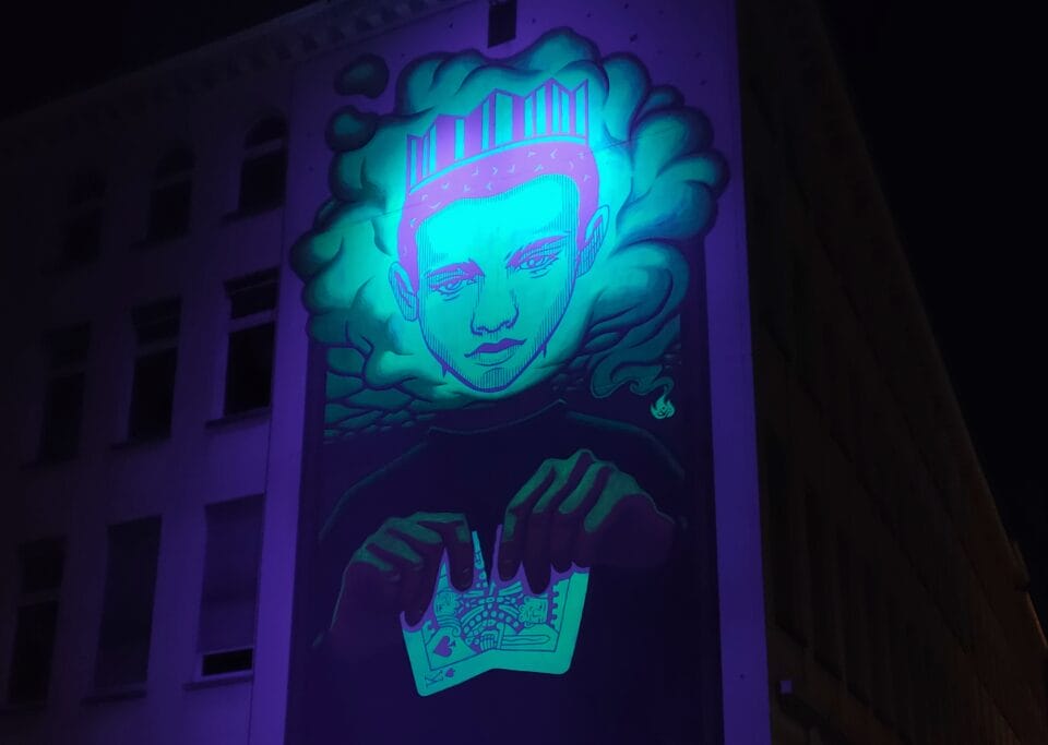 a glow-in-the-dark mural of a man in a crown ripping a playing card in half