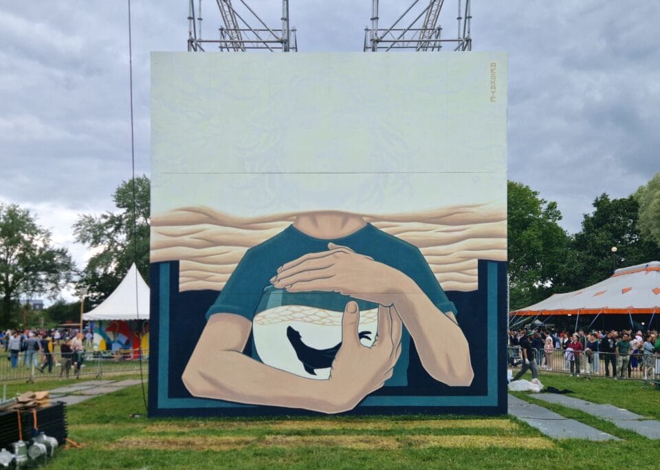 a glow-in-the-dark mural during the day, exhibiting only the bottom half of a figure holding a fishbowl
