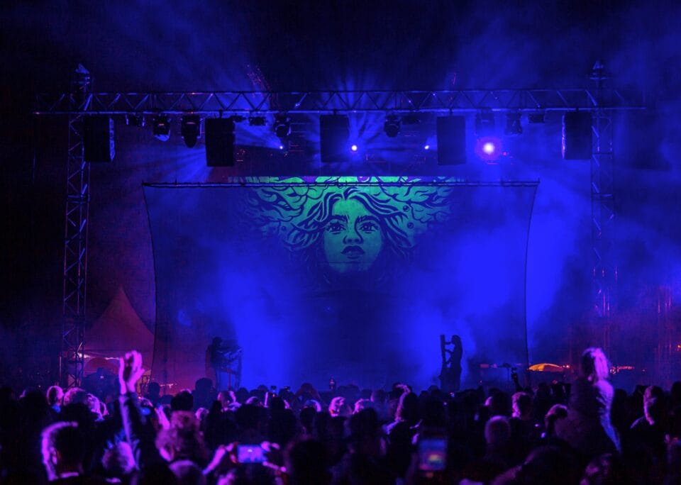 a glowing mural depicting the face of a young woman is the a backdrop of a concert stage