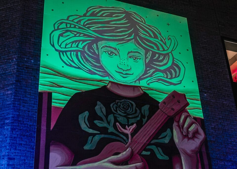 a glow-in-the-dark mural on the side of a building, depicting a figure holding a ukulele