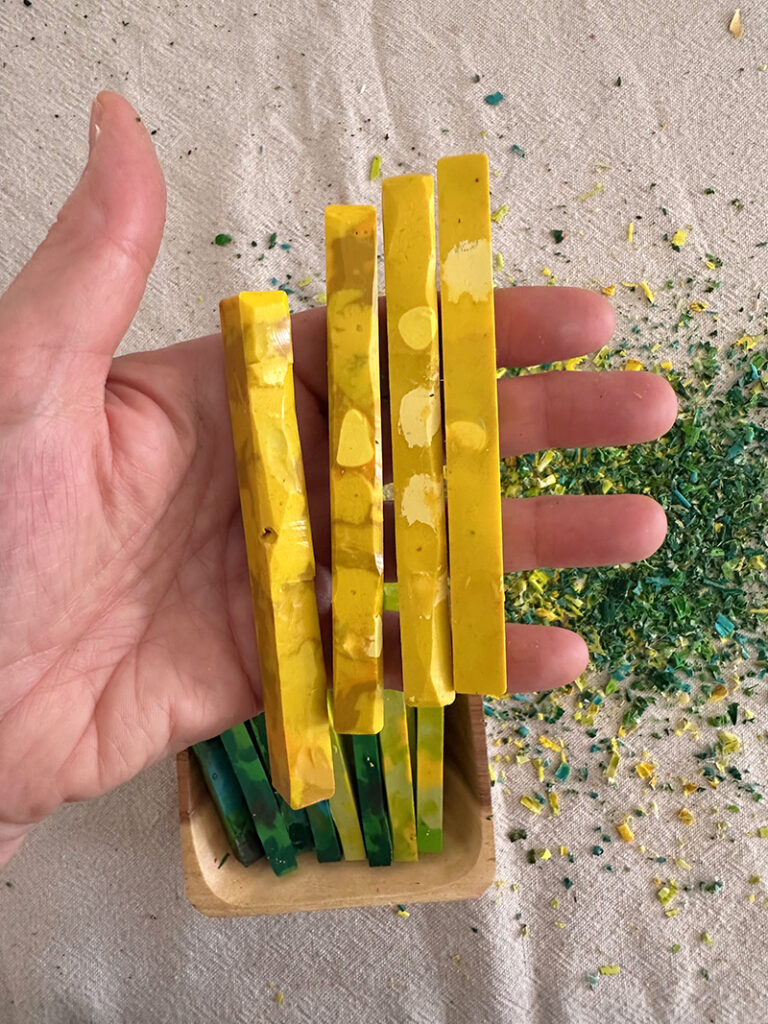 Four homemade yellow crayons in a hand, showing size.