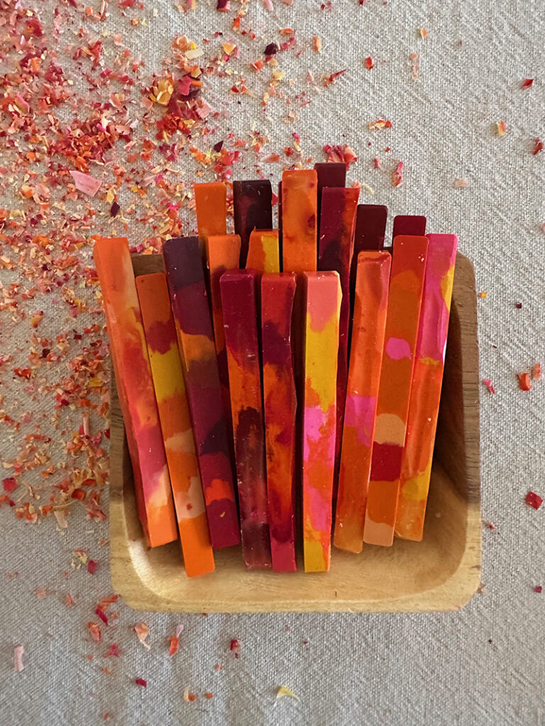 A small wooden bowl holding a set of homemade crayons in red and orange hues.