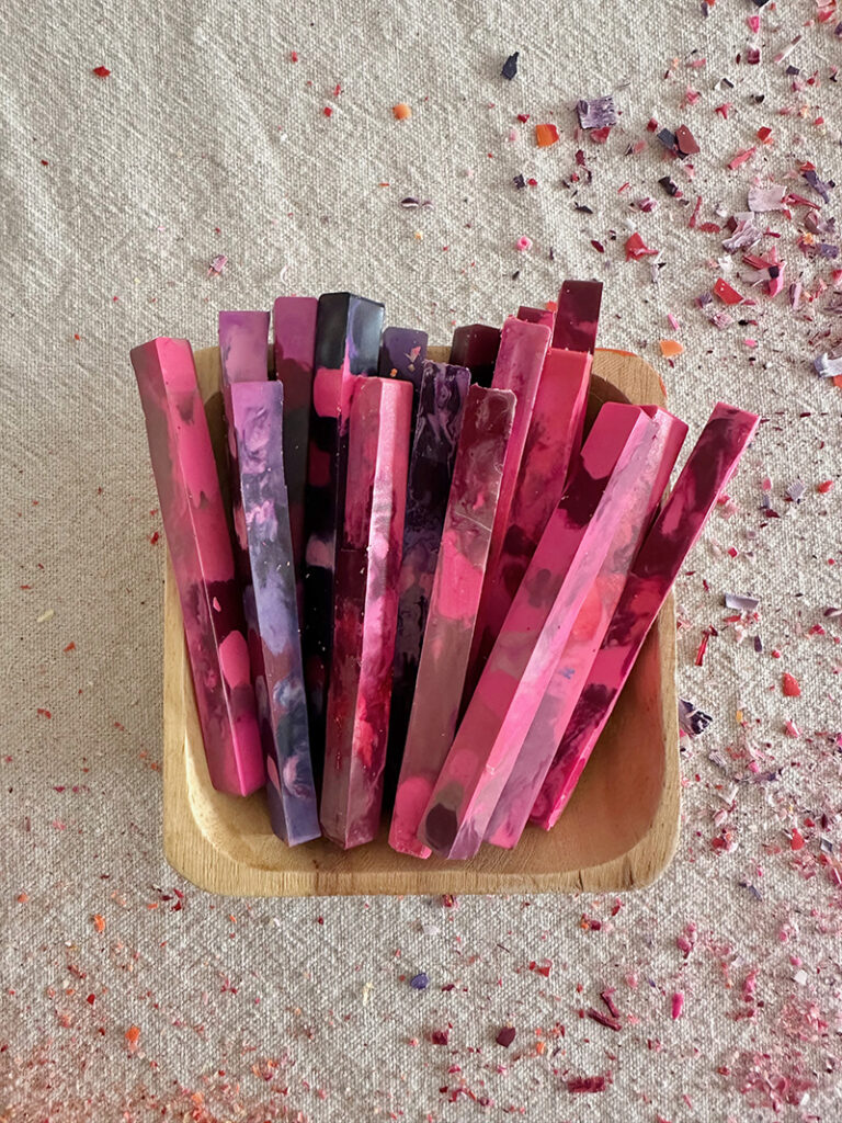 A small wooden bowl holding a set of homemade crayons in pink and purple hues.