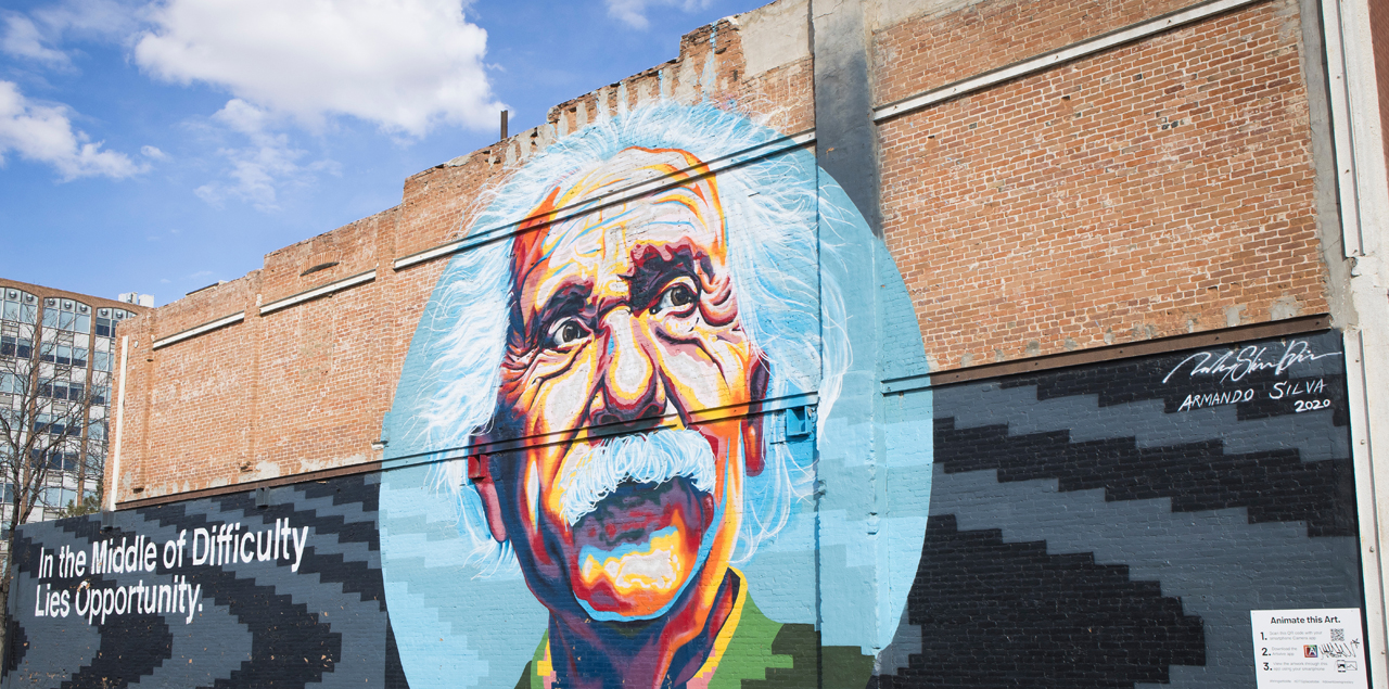 A colorful mural depicting Albert Einstein on a dark wall.