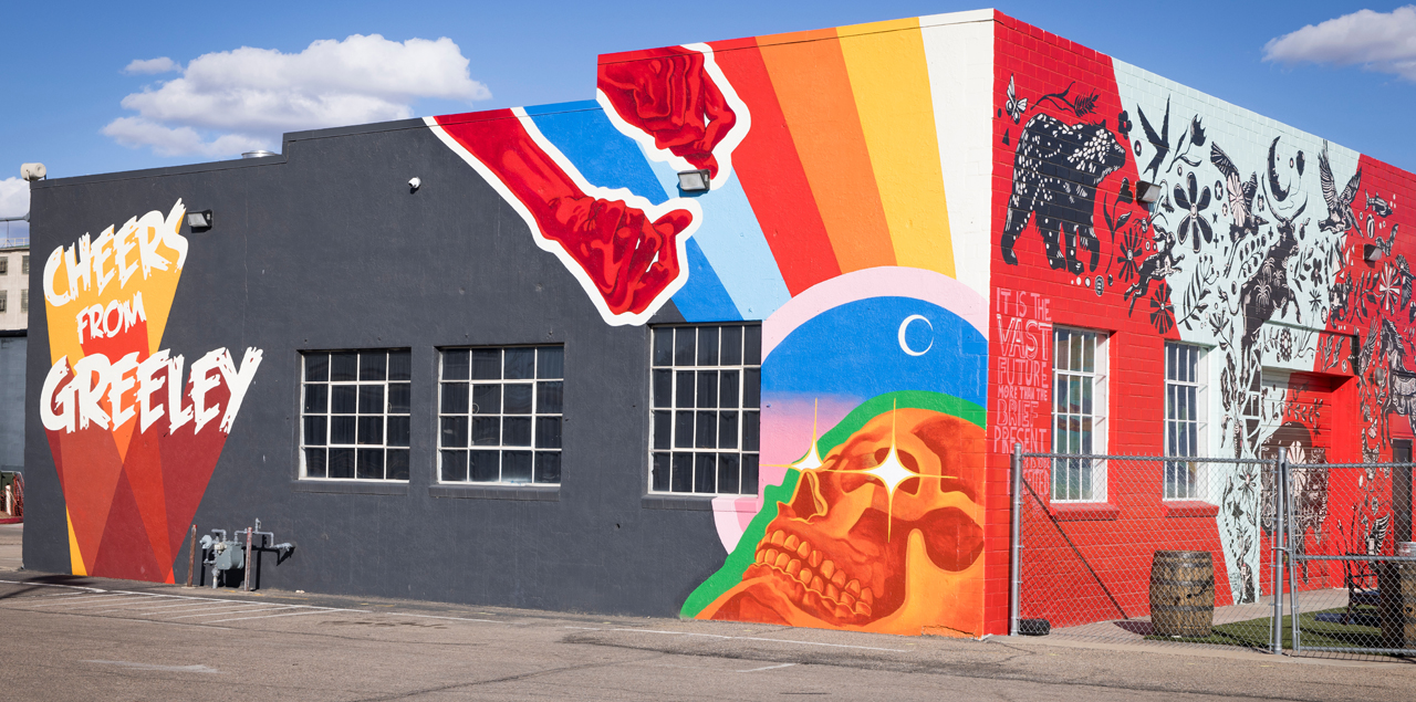 Colorful mural depicting a pair of hands reaching down toward an organge skull.