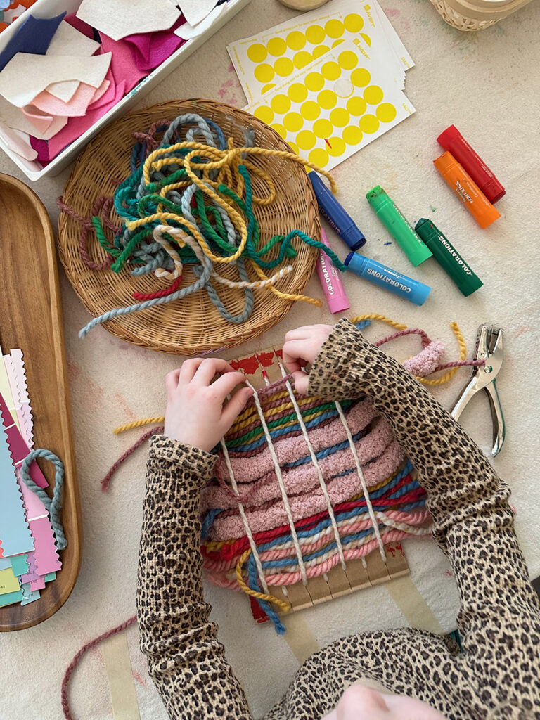Young child weaving on a cardboard loom with different yarns.