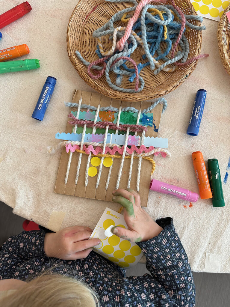 Child embellishing their cardboard loom weaving with yellow dot stickers.