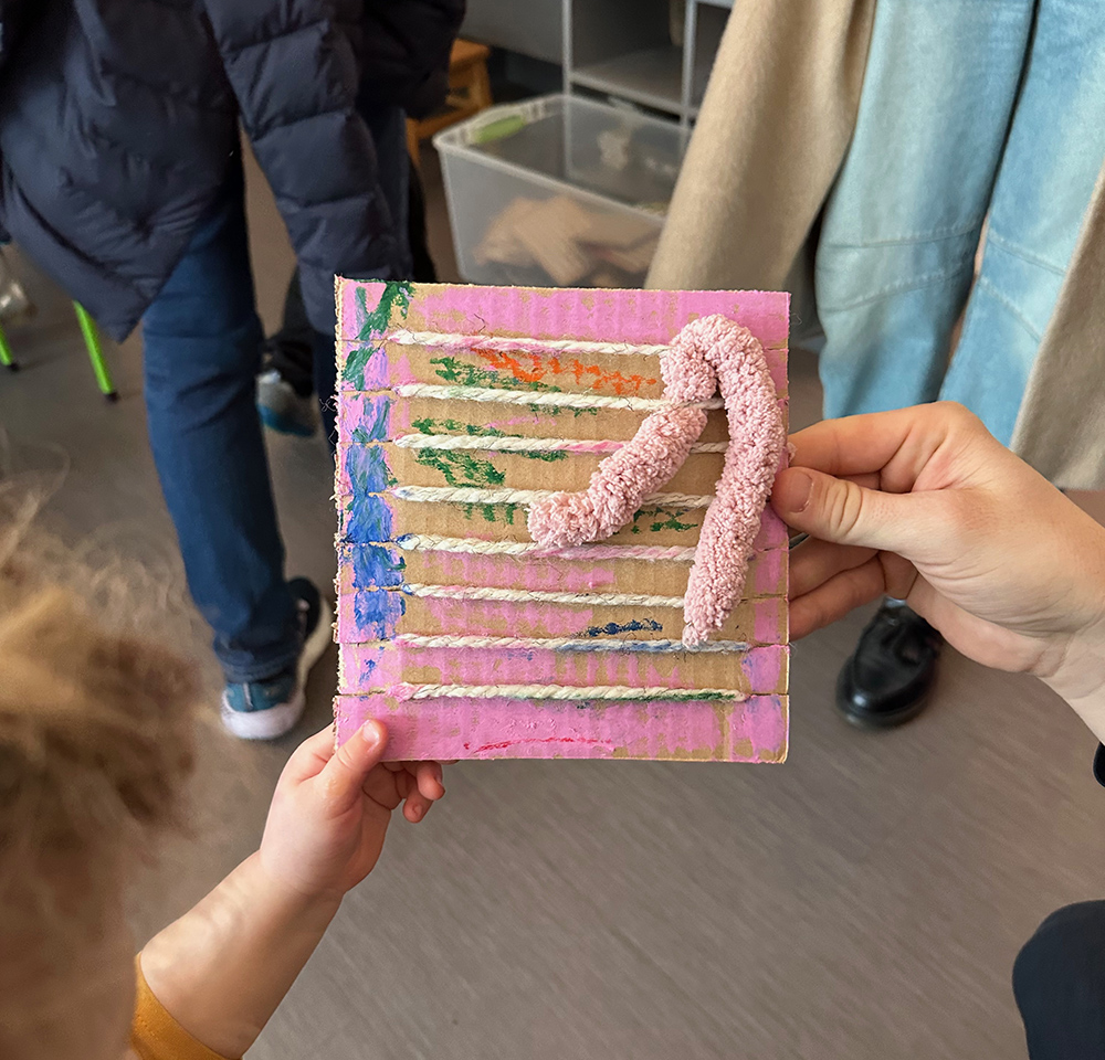 Child holding up her cardboard loom weaving with one pink piece of thick, chenille yarn.