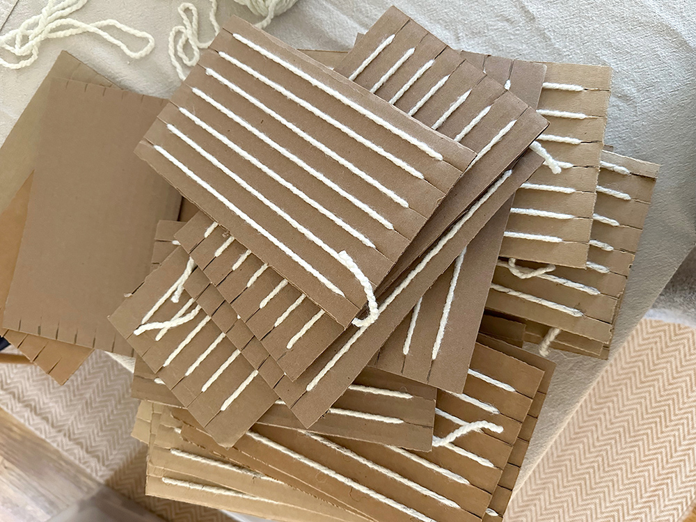 A pile of cardboard weaving looms, some have a yarn warp and some are empty.