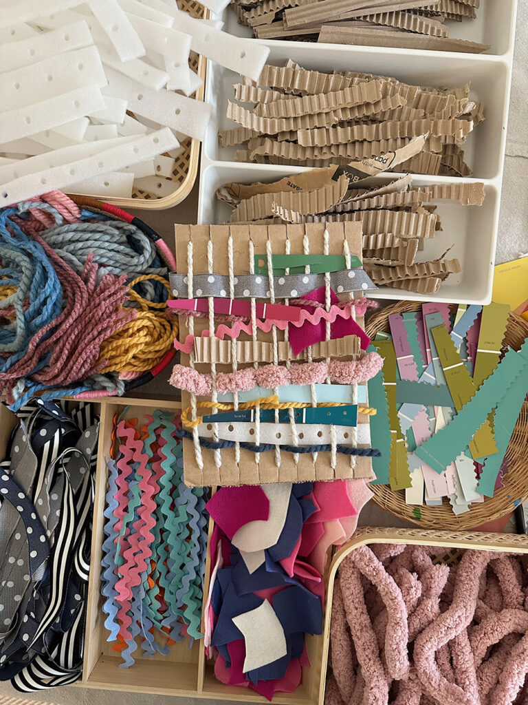 Table full of different materials and textures to use in weaving with a cardboard loom.