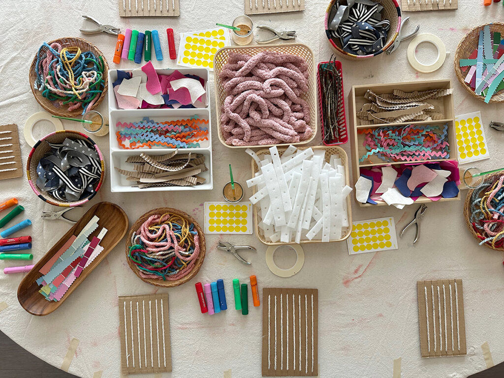 A table set up with cardboard looms and weaving materials ready for children to come and use.